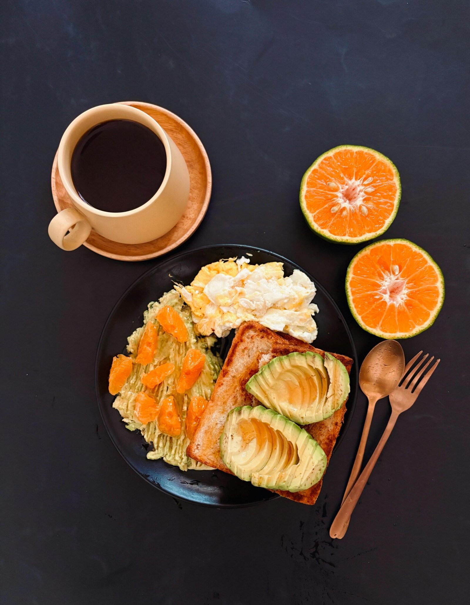 A flat lay of a nutritious breakfast with avocado toast, oranges, and black coffee.