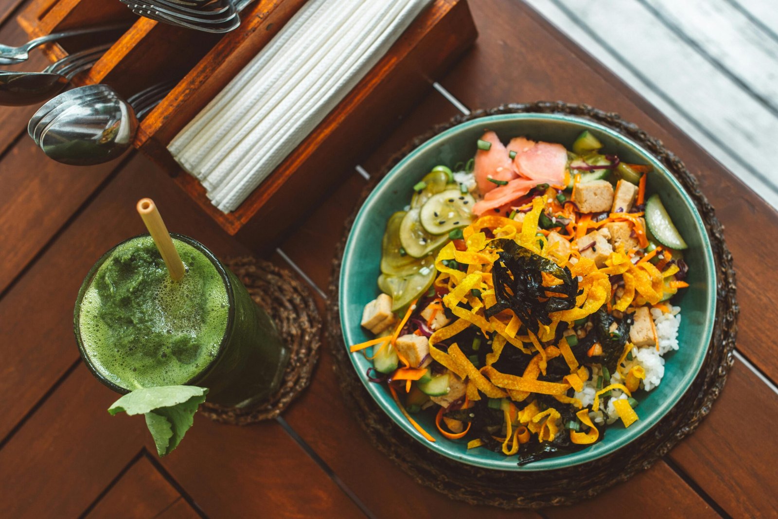 Top view of a colorful vegetarian bowl with a refreshing green juice on a wooden table, perfect for healthy lifestyle content.